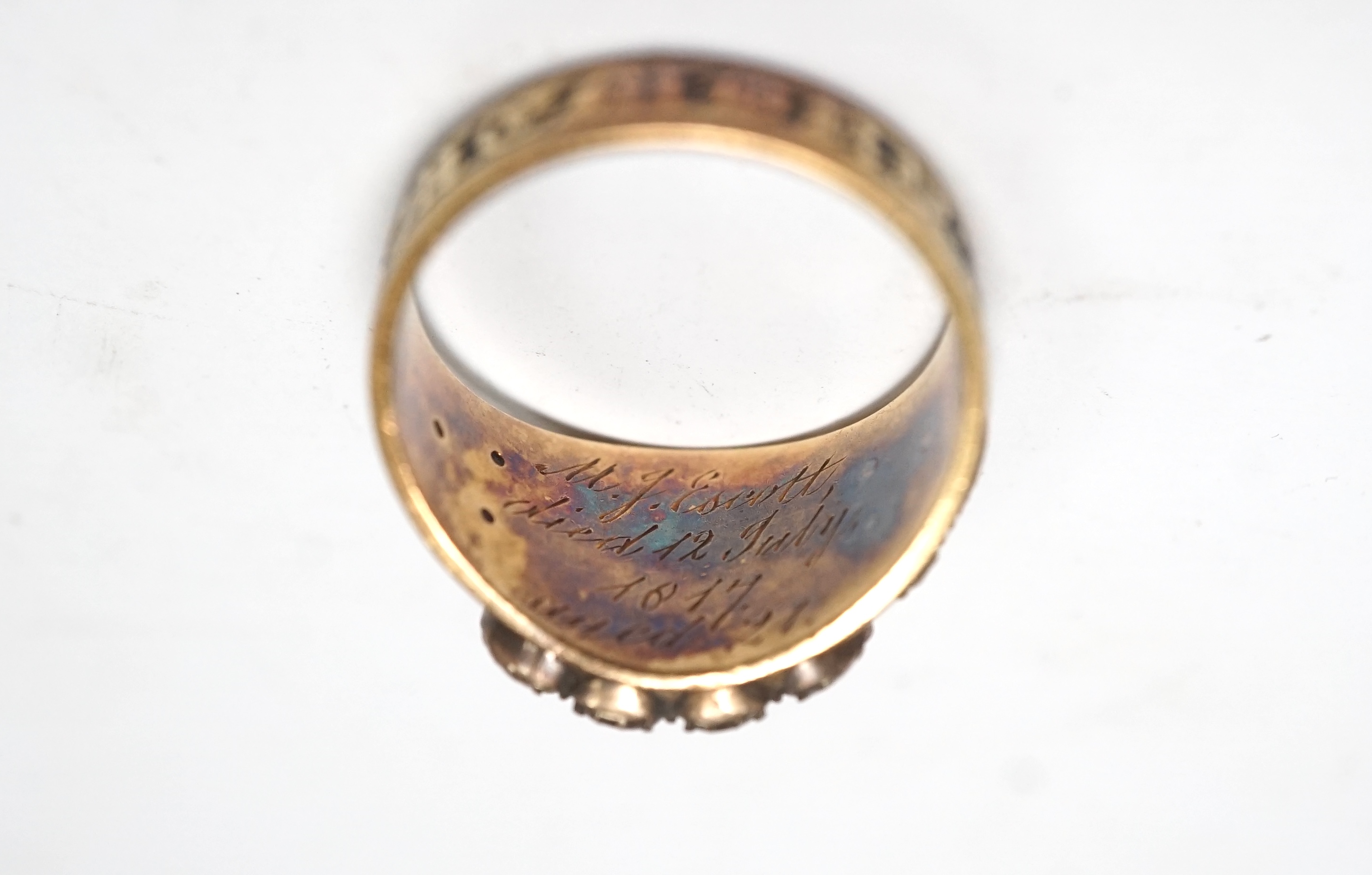 A late George III yellow metal, two colour enamel and split pearl set mourning ring, with plaited hair beneath a glazed panel, inscribed, 'M.J. Escott died 12th July, 1817 aged 21', size N, gross weight 6.8 grams. Condit